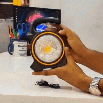 ForKumi solar USB camping lantern held by hands with built-in handle and USB charging cable on table