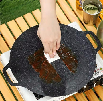 ForKumi 30cm Japanese nonstick skillet with speckled surface being cleaned by hand on wooden table