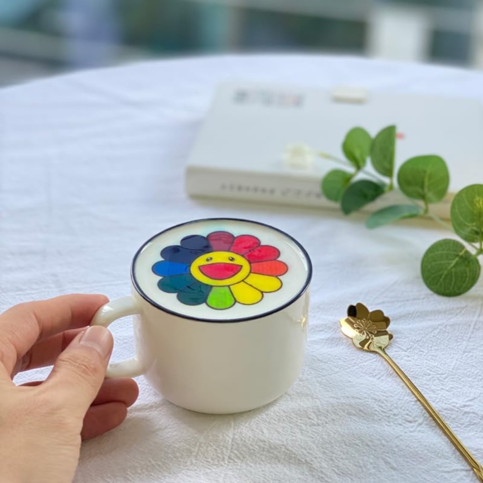 White coffee cup with colorful custom coffee art printer flower design on foam held by hand on white table