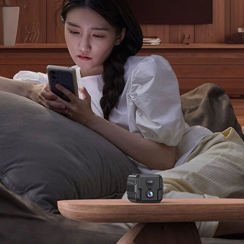 ForKumi HD WiFi security camera placed on wooden table with woman using smartphone in background