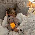 Woman cuddling a glowing plush musical otter soother for babies in bed with cozy bedding
