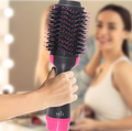ForKumi 1000W hot air brush styler held in hand with black and pink bristles and blurred background