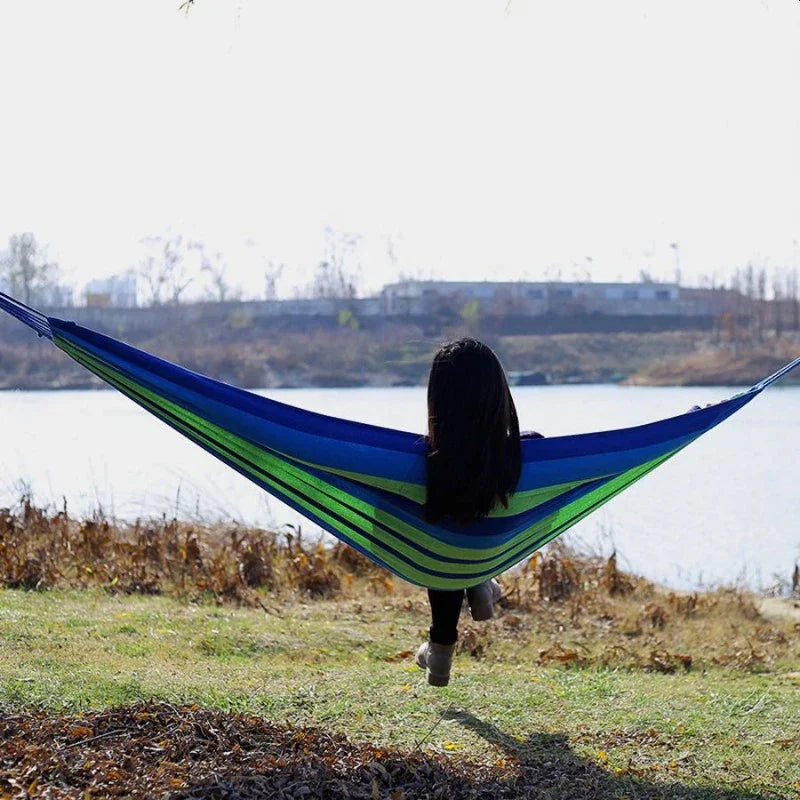 ForKumi colorful striped single person outdoor hammock hanging between trees in a sunny garden