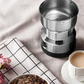 ForKumi small electric grinder for home with stainless steel bowl next to coffee cup and beans