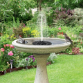 ForKumi solar fountain outdoor garden birdbath with water spray surrounded by flowers and greenery