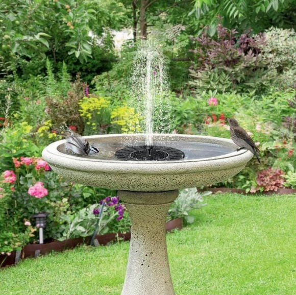 ForKumi solar fountain outdoor garden birdbath with water spray surrounded by flowers and greenery