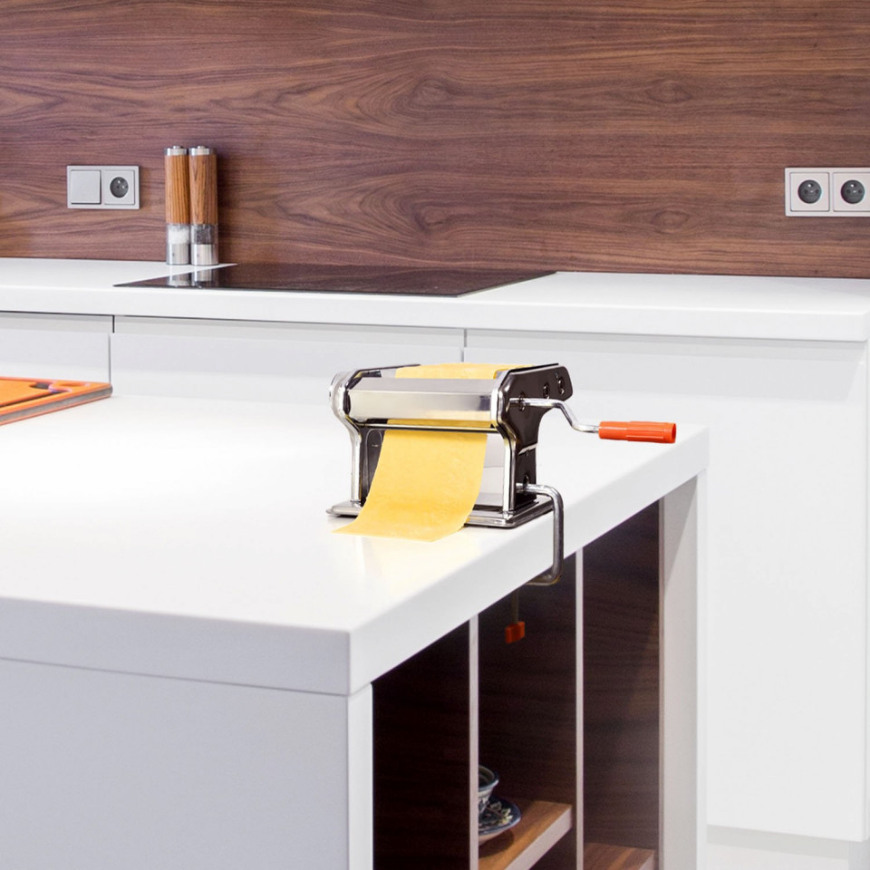 ForKumi stainless steel pasta maker with orange handle on kitchen countertop rolling fresh pasta dough