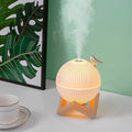 ForKumi ultrasonic humidifier with essential oils emitting mist on wooden stand beside cup and plant