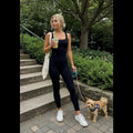 Woman wearing Avis black tummy control jumpsuit walking a small dog outdoors with coffee cup